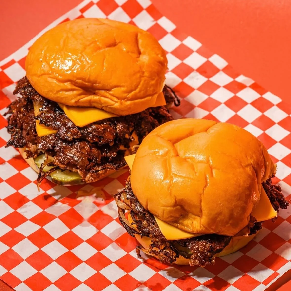 Deux smash burgers cheddar sur papier damier rouge et blanc